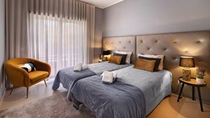 Een moderne hotelkamer met een groot bed, een bank, een bijzettafeltje met een lamp en lichte gordijnen.
