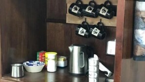Um armário de madeira com uma placa com o tema café acima, contendo uma chaleira, uma cafeteira e vários itens relacionados a café.