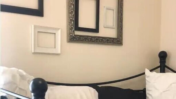 Cama com estrutura metálica preta e roupa de cama branca.