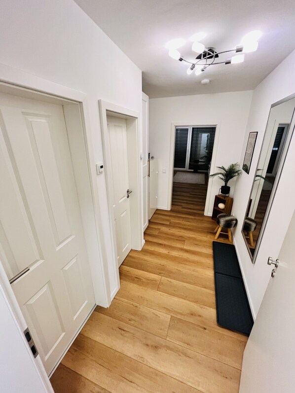 A hallway with wooden flooring, white walls, and a ceiling light fixture.
