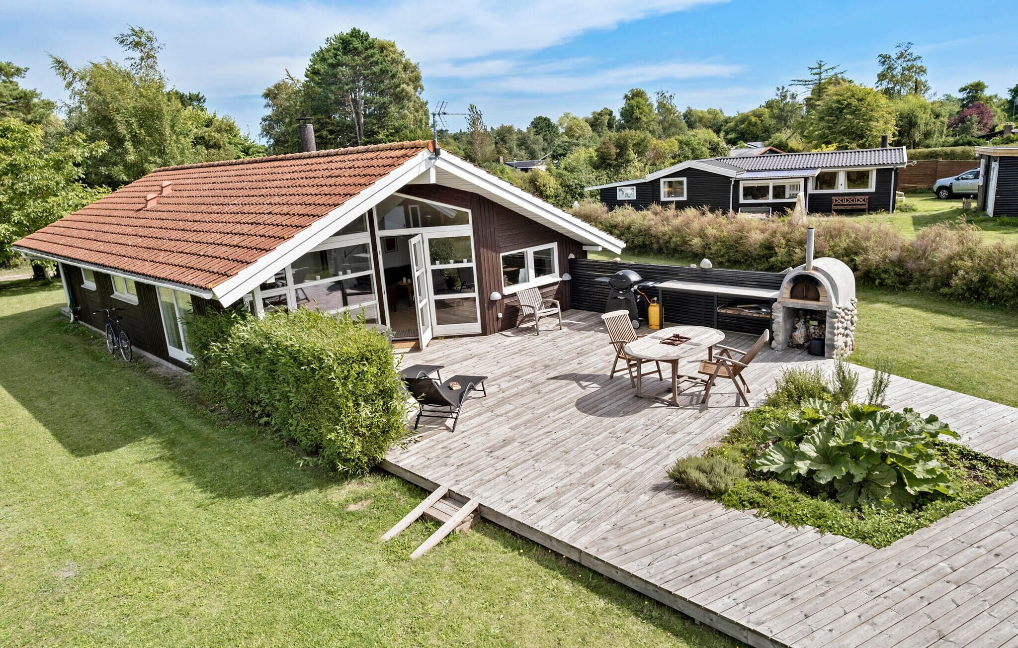 A wooden deck with outdoor furniture, a barbecue area, and a stone oven.