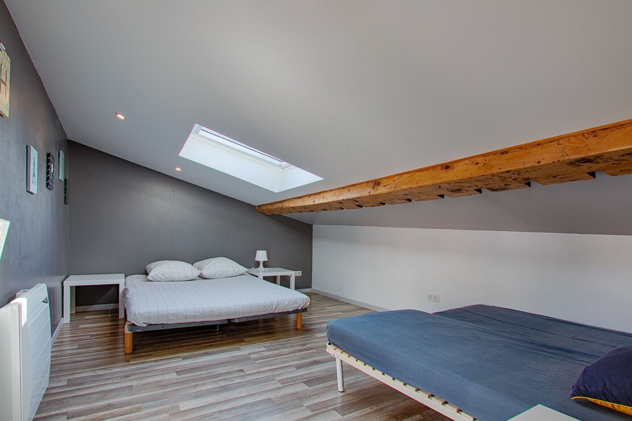 A bedroom with a sloped ceiling, a skylight, a bed, a bedside table, and a small desk.
