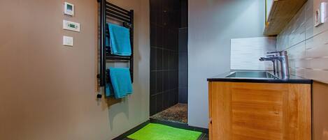 Een badkamer met een douche, een handdoekrek met blauwe handdoeken, een groene mat en een houten kastje.