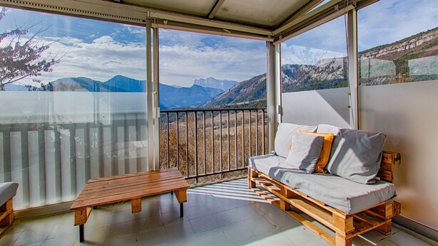 Ein Balkon mit einer Couch und einem Tisch, mit Blick auf die Berge.