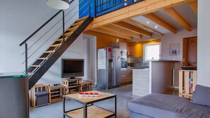 Ein moderner Wohnraum mit Treppe, Fernseher, Küchenzeile und einer Couch.