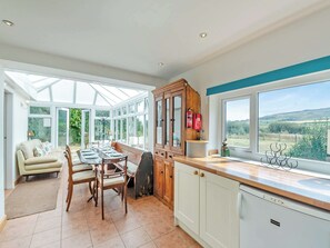 A conservatory with a dining table and chairs, a sofa, and wooden cabinets.