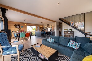 A modern living room with a sofa, coffee table, and patterned chairs. A staircase with a railing leads to a kitchen area. - Holiday Home 'Gite Ty Laouen' with Private Terrace and Wi-Fi (SARZEAU)