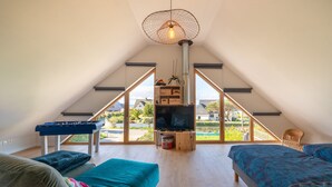 A spacious attic bedroom with a large window, a television, a foosball table, and a cozy seating area. - Holiday Home 'Gite Ty Laouen' with Private Terrace and Wi-Fi (SARZEAU)