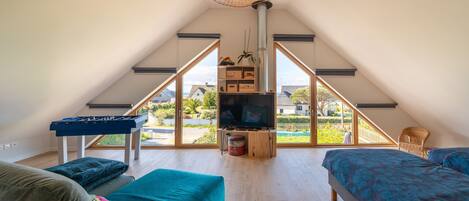 A spacious attic bedroom with a large window, a television, a foosball table, and a cozy seating area.