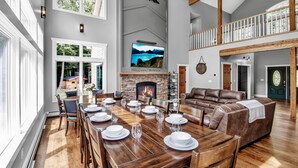 A spacious living area with a fireplace, a dining table set for six, and a large window overlooking a scenic landscape.