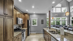 A modern kitchen with wooden cabinets, stainless steel appliances, and a large window providing a view of the outdoors.