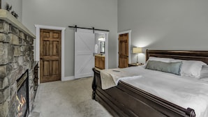 A bedroom with a stone fireplace, wooden doors, a bed with white bedding, and a nightstand with a lamp.