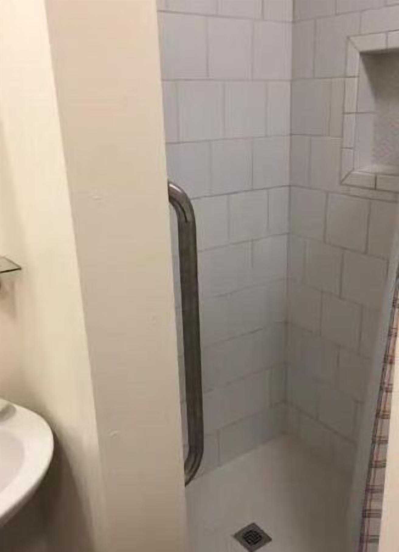 Et lille badeværelse med hvide fliservægge, et hvidt håndvaskarrangement og en brusekabine med glasdør.