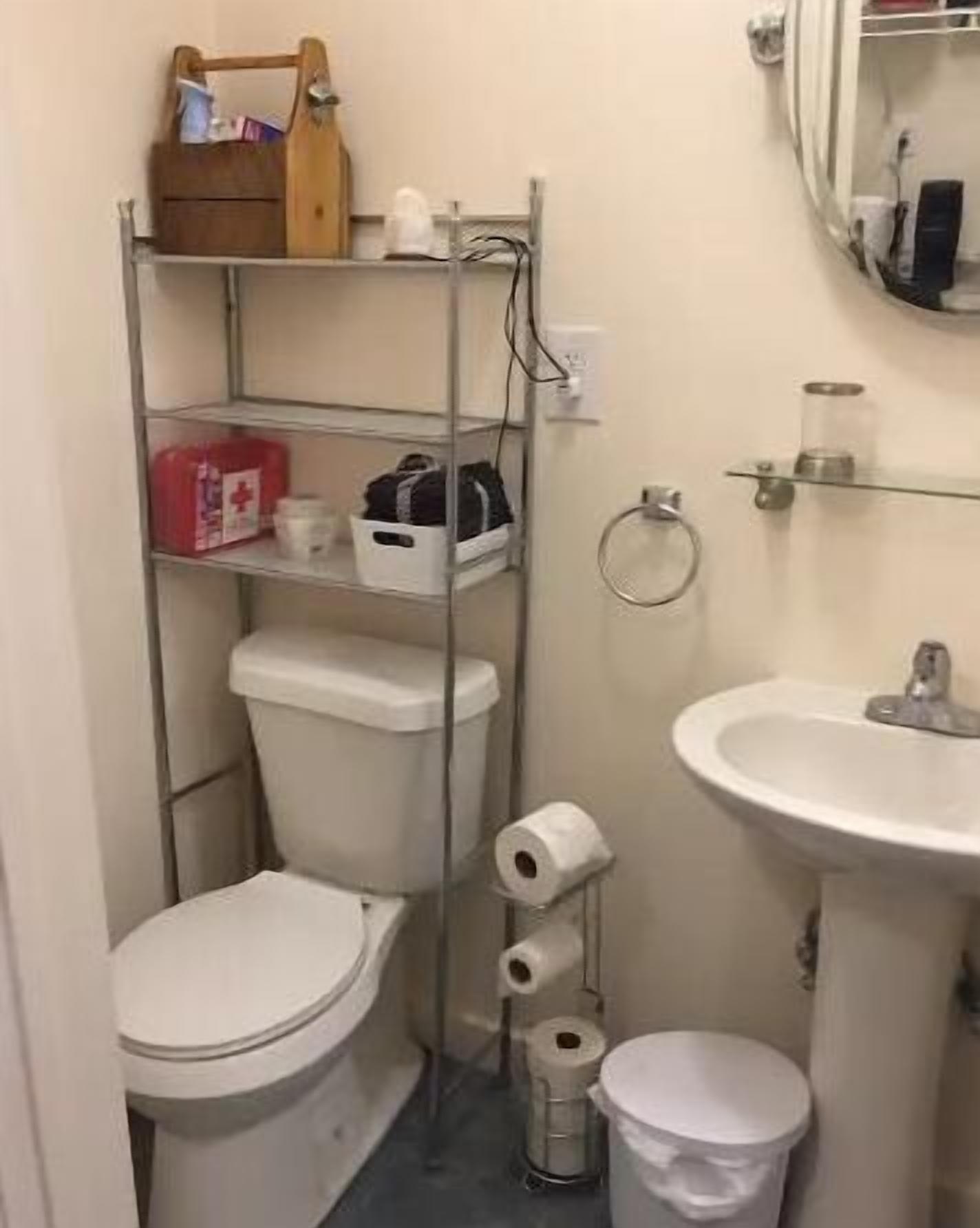 Un baño pequeño con inodoro, un estante con artículos de aseo, un lavamanos y un cubo de basura.