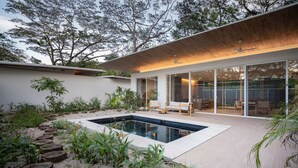 A modern house with a swimming pool, wooden deck, and glass doors leading to a patio area.