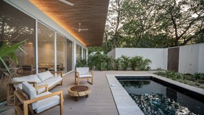 A modern outdoor patio with a pool, wooden furniture, and large glass doors.