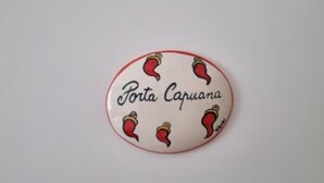A round, oval-shaped object with the text "Porta Capuana" and illustrations of red chili peppers. - The Fondaco At The Historical Archives (Napoli)