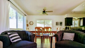 Un salon avec deux canapés sombres, une table à manger en bois et un ventilateur de plafond.