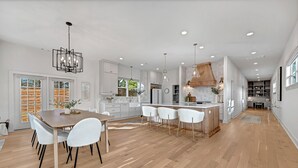Una cocina amplia con muebles blancos, una mesa de comedor de madera y una isla central con taburetes de bar.