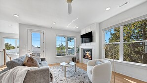 Una sala de estar moderna con chimenea, ventanas amplias y un ventilador de techo.