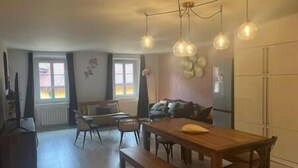 A spacious living area with a wooden dining table, benches, a sofa, and a large window providing natural light.
