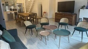 A living room with a sofa, three round tables, and a TV. There is a staircase leading to a kitchen.