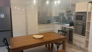 A modern kitchen with white cabinets, a wooden dining table, and pendant lighting.