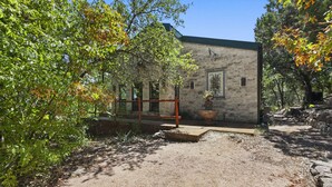 Un bâtiment rustique en pierre, doté d’un toit végétalisé, entouré d’arbres et bordé d’un chemin de gravier.
