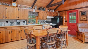 A rustic cabin interior with wooden cabinetry, a dining table with chairs, a red door, and a leather chair. - Lakefront Cabin/ 314`  Shoreline (Stoddard)