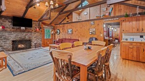 A rustic cabin interior with a stone fireplace, wooden dining table, and a cozy seating area. - Lakefront Cabin/ 314`  Shoreline (Stoddard)
