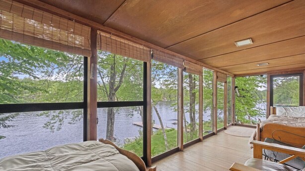 A room with a bed and a desk, large windows with a view of a lake and trees. - Lakefront Cabin/ 314`  Shoreline (Stoddard)