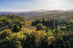A yellow villa surrounded by lush greenery and hills.