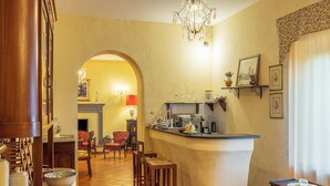 A kitchen with a bar area, wooden chairs, a chandelier, and a fireplace.