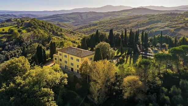 Une villa jaune, entourée d’une végétation luxuriante et de collines.