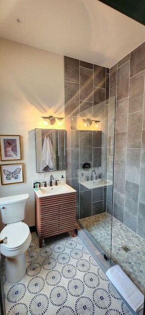 Un baño con inodoro, lavabo, tocador, ducha y baldosas de suelo estampadas.