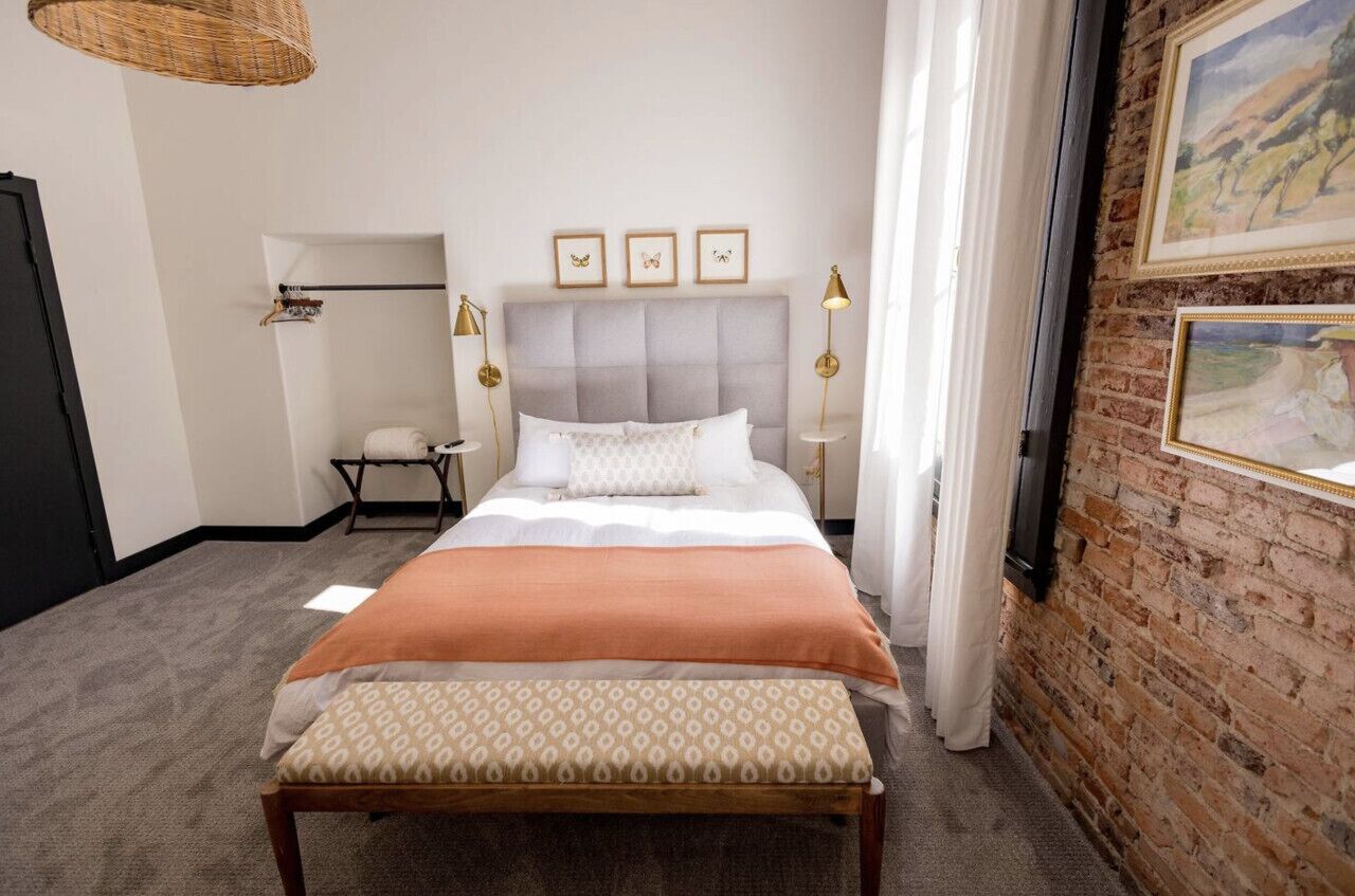 A neatly arranged bedroom with a bed, bedside tables, a bench, and artwork on the walls.