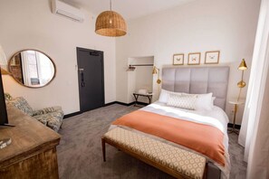 Un dormitorio con cama, lámparas de noche, un espejo, un tocador y un banco.