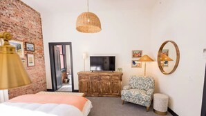 Une chambre avec un lit, une télévision, une lampe en osier, un fauteuil à motifs et un miroir.