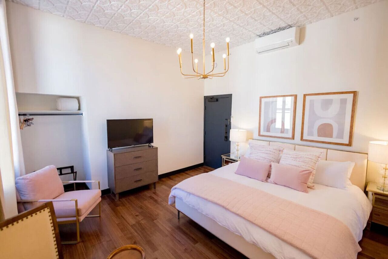 Un dormitorio con una cama, televisión, cómoda, una silla y una araña.