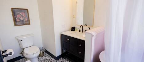 A bathroom with a toilet, sink, mirror, and shower curtain.