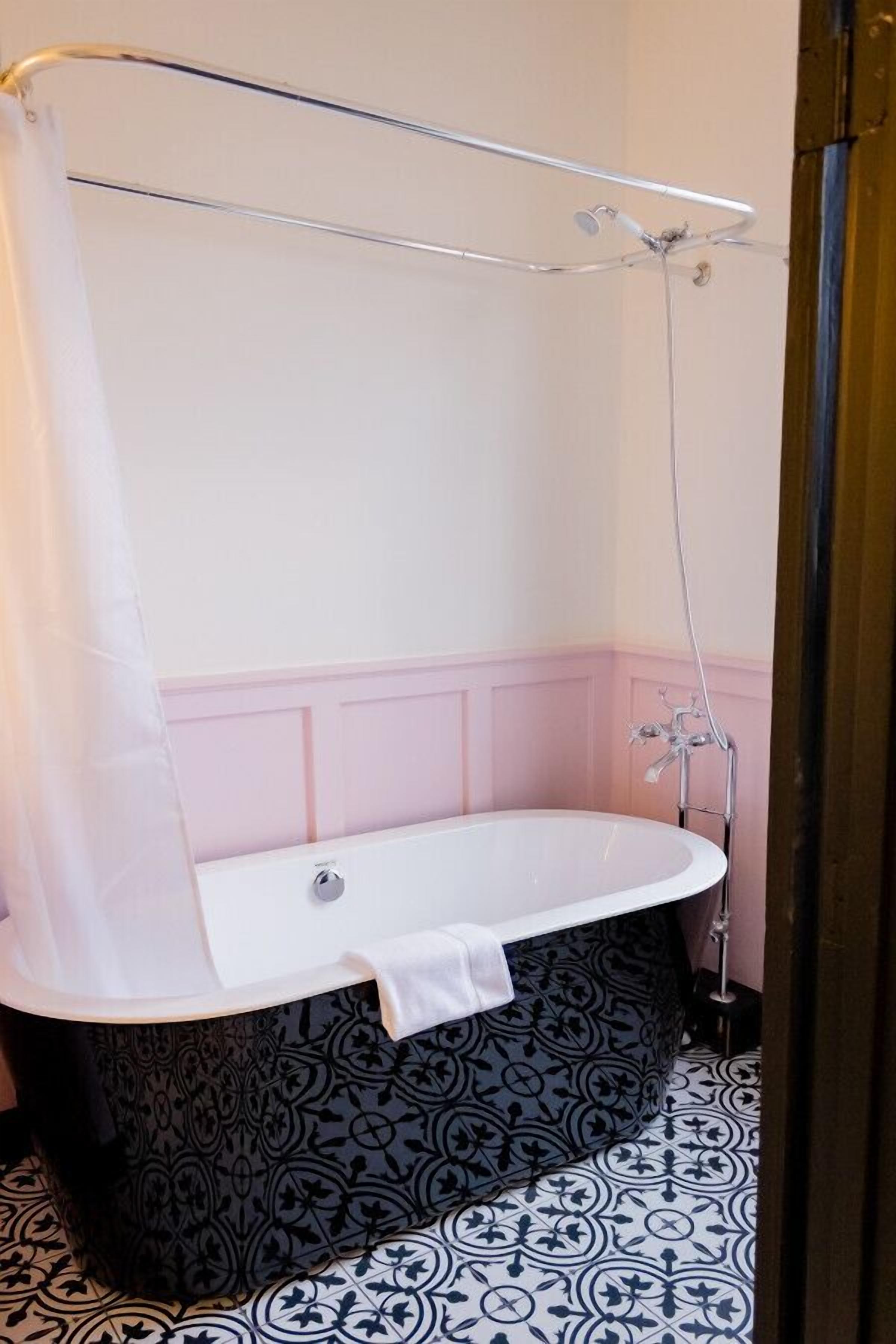 A bathroom with a freestanding bathtub, a shower curtain, and a patterned floor.