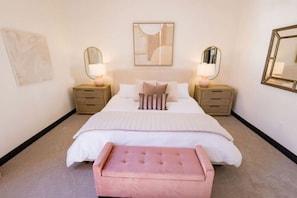 Ein Schlafzimmer mit einem Bett, Nachttischen, Lampen, einer Bank und Kunstwerken an den Wänden.