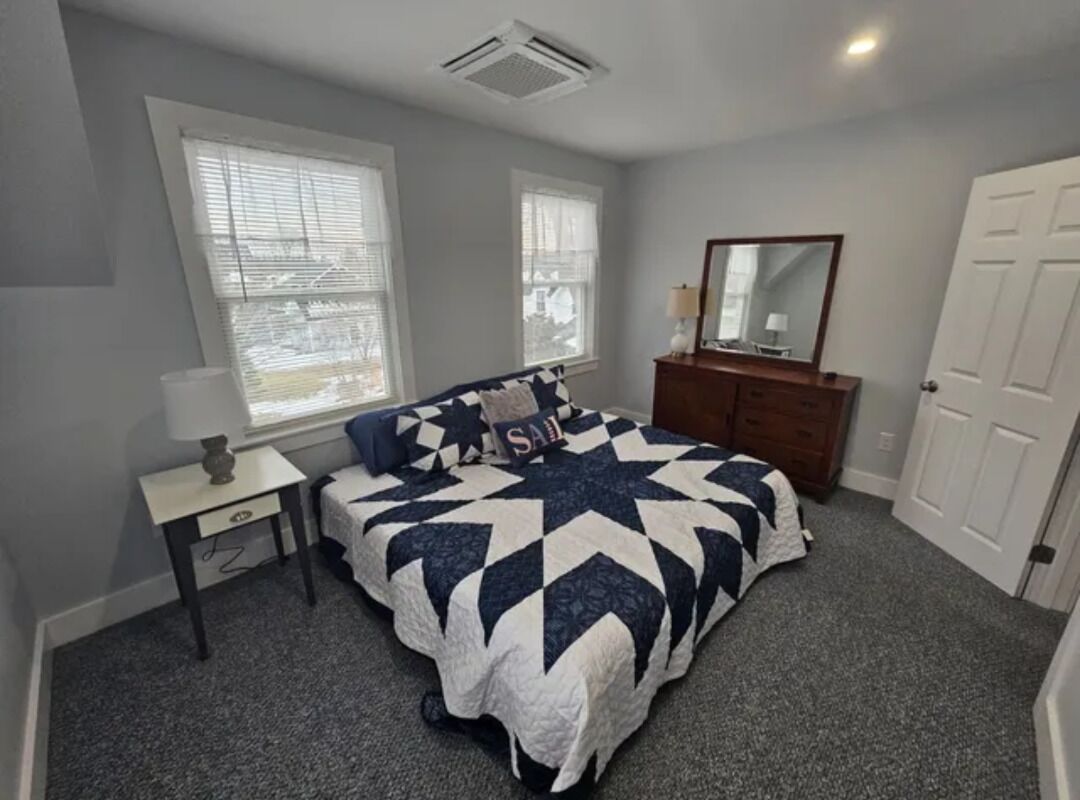 A bedroom with a bed, a dresser, a nightstand, and a window.
