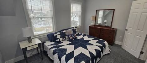 A bedroom with a bed, a dresser, a nightstand, and a window.