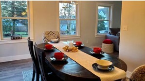 Uma área de refeições com uma mesa de madeira escura posta para quatro pessoas, tigelas vermelhas e brancas e um jogo de sousbacias tecido.