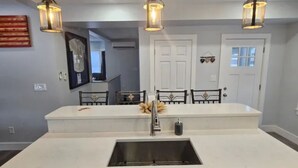 Uma cozinha moderna com uma ilha central, iluminação pendente e uma área de jantar com cadeiras.