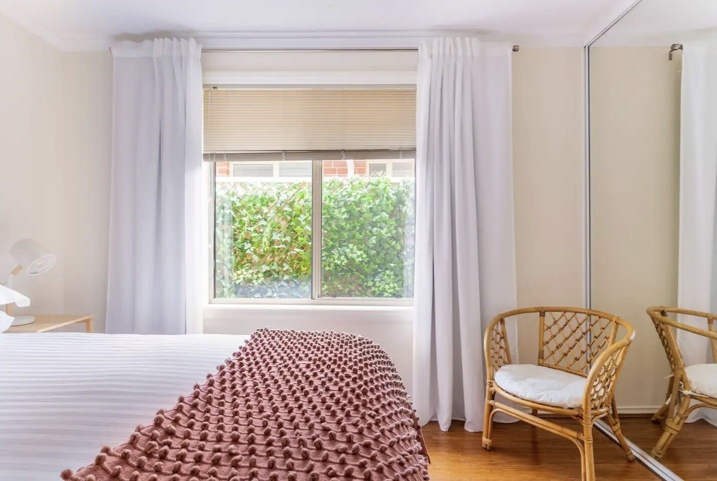 Une chambre avec un grand lit, une fenêtre avec des rideaux, une chaise et un miroir.