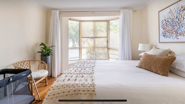 Un dormitorio con una cama grande, una silla, una planta en maceta y una ventana con cortinas.