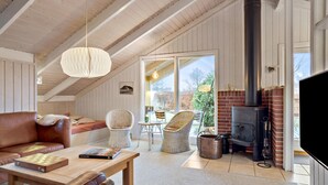 A cozy loft-style room with a wooden ceiling, a large window, a fireplace, and a television.