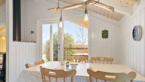 A dining area with a table and chairs, a hanging light fixture, a clock on the wall, and a view through the door.